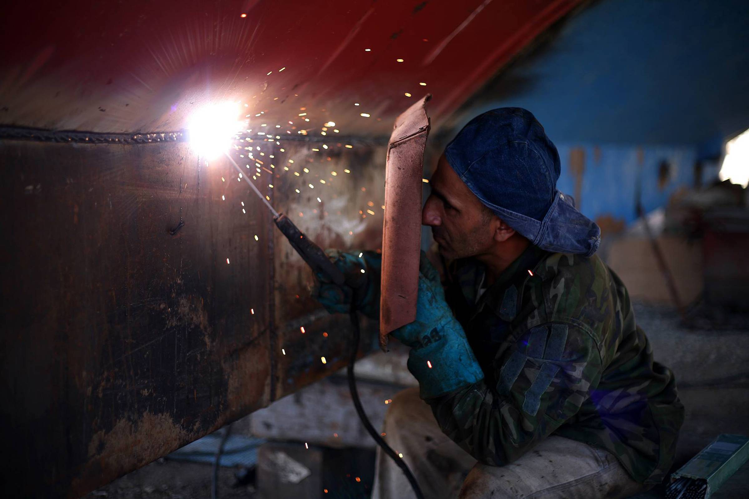 A welder at work on a steel section, sparks falling, seen close.