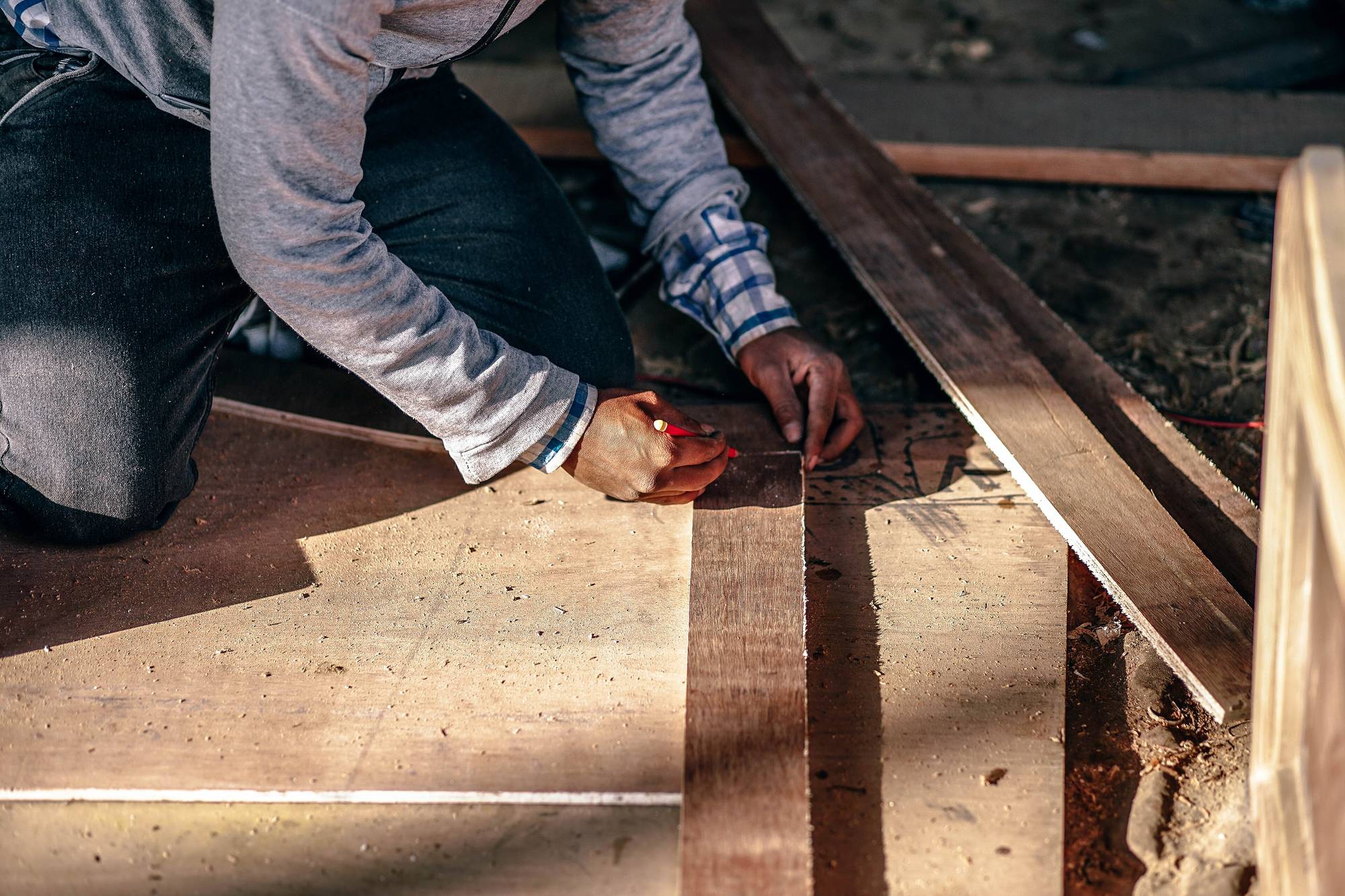 Hands running a hand plane along a length of timber in raking afternoon light.