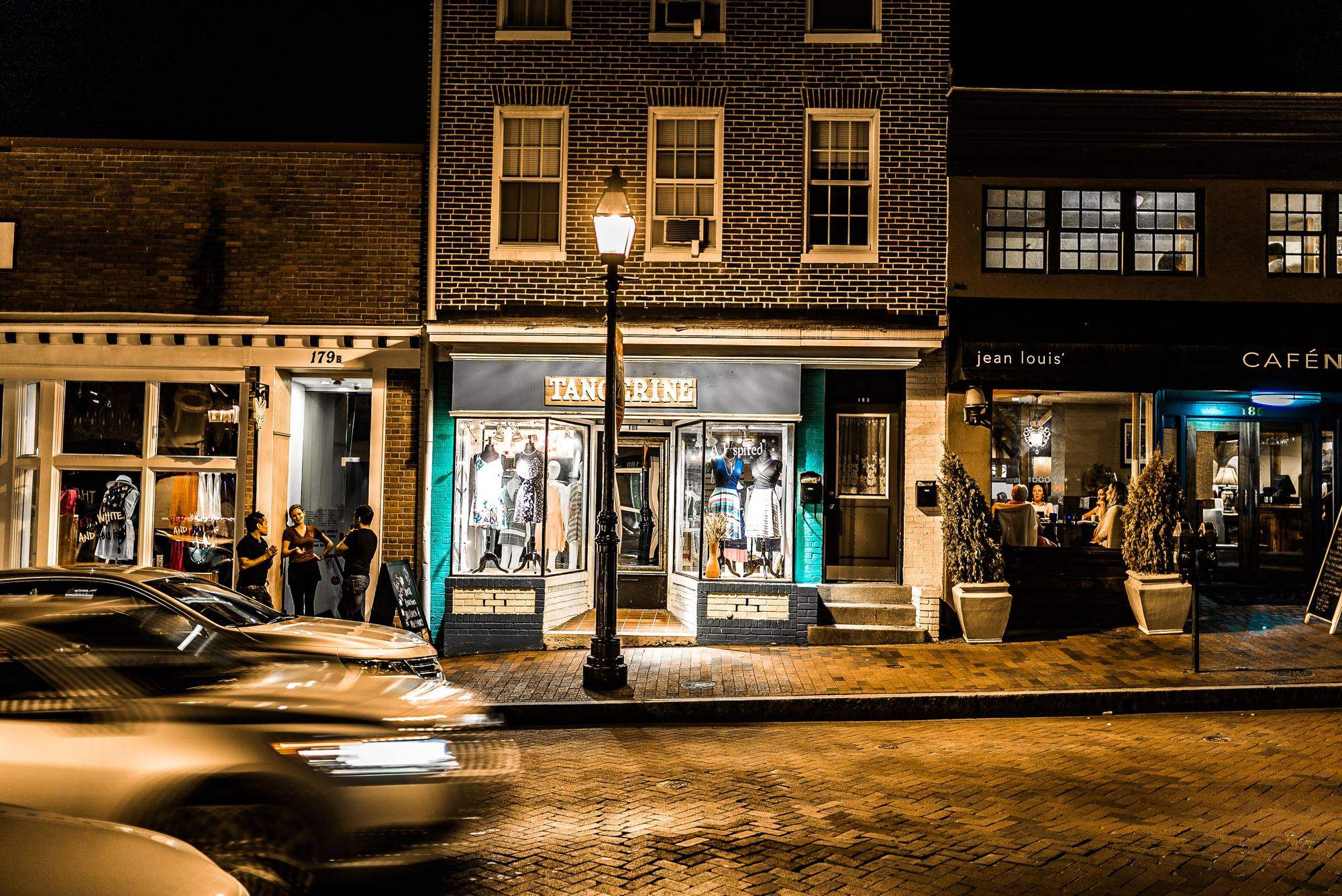 A short row of shopfronts on a small-town street at dusk, windows lit from inside.