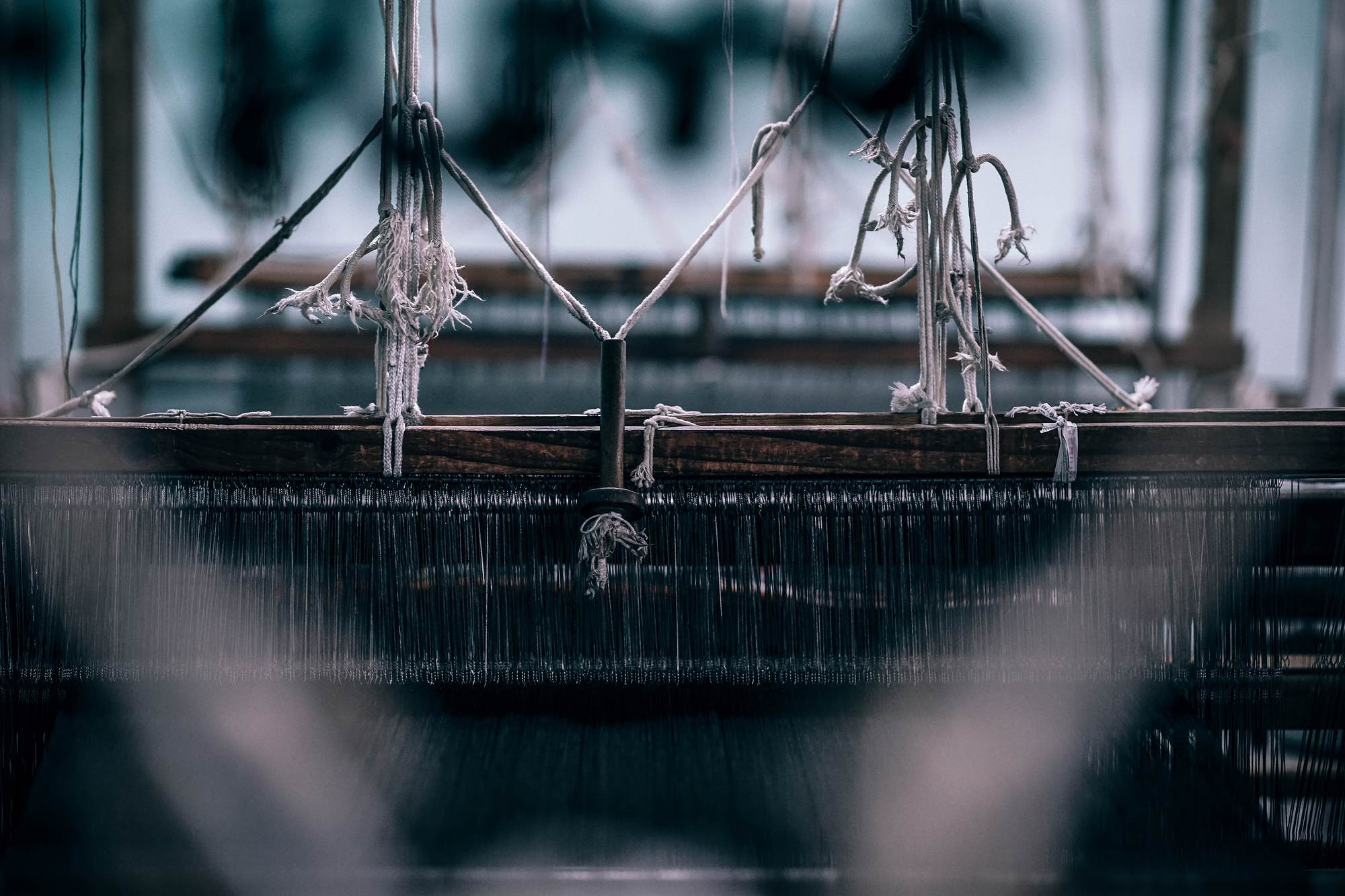 A long row of industrial looms receding down a factory floor under high windows.