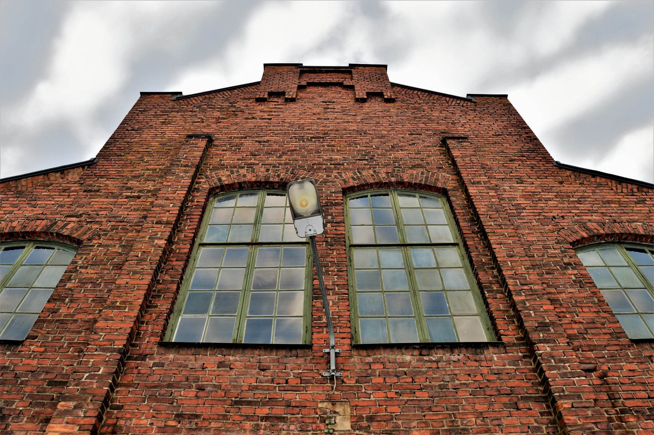 A tall brick works building with arched factory windows, seen from below against open sky.