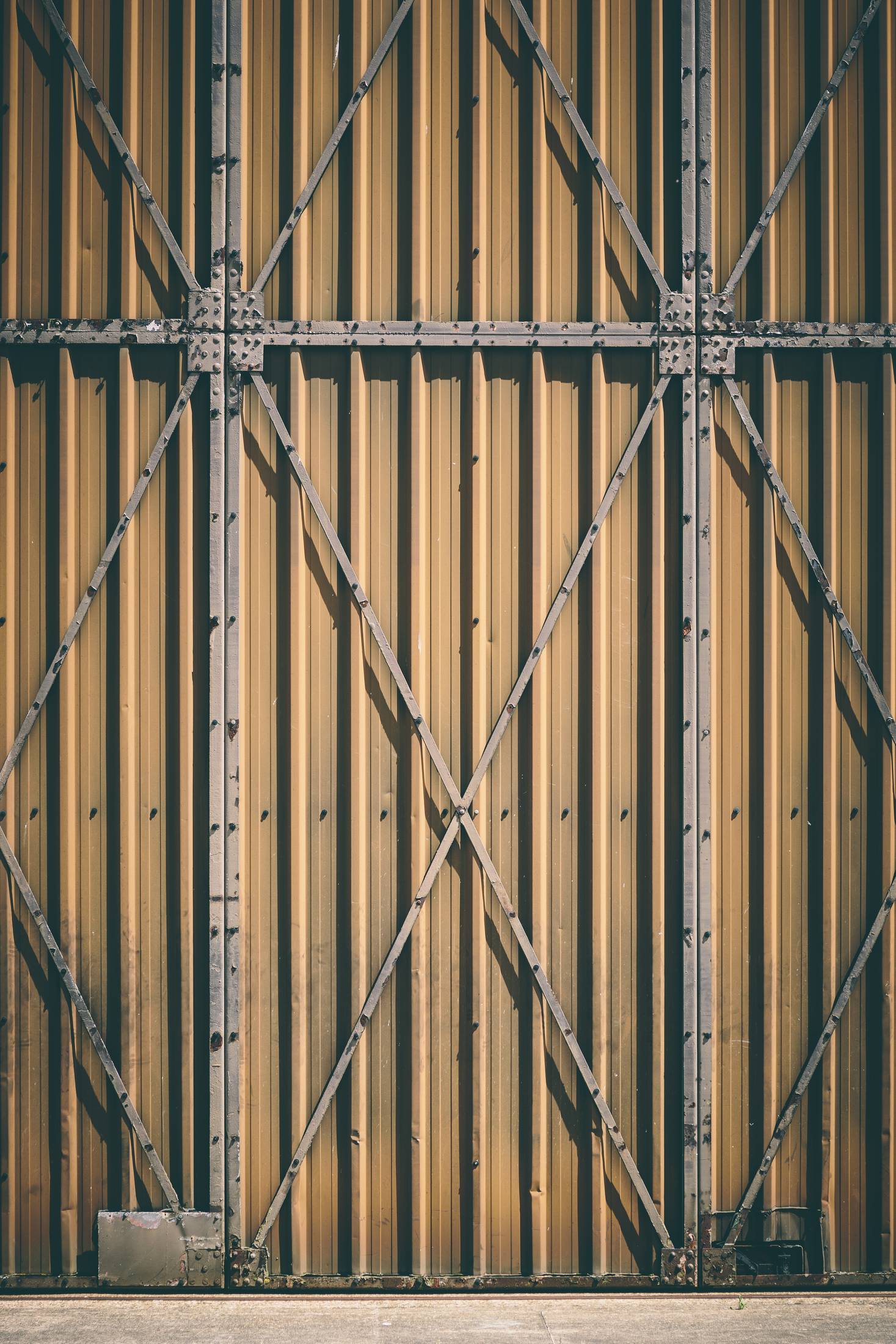 Tall braced industrial door in weathered timber and steel, closed, photographed square on.